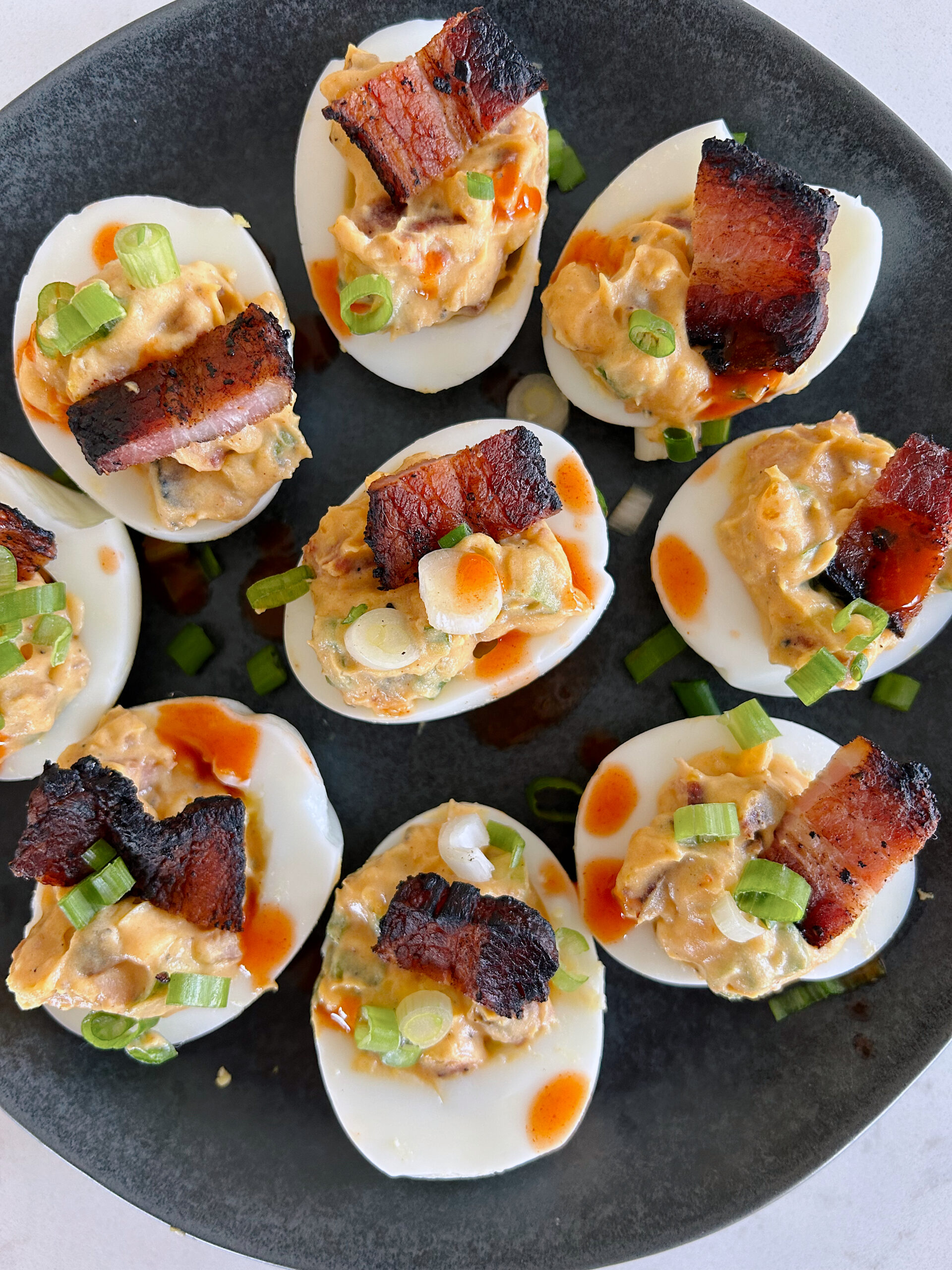 hard boiled eggs with bacon and green onions on a black plate