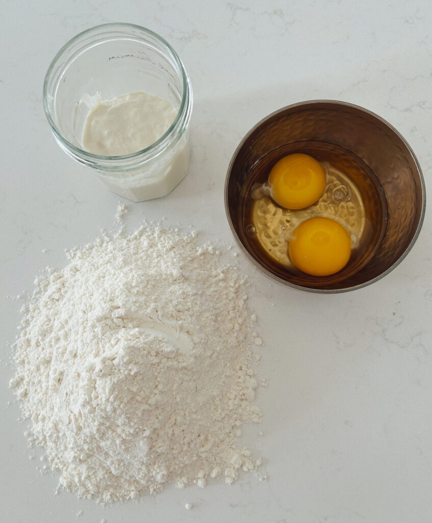 eggs, flour and sourdough starter on a white counter top