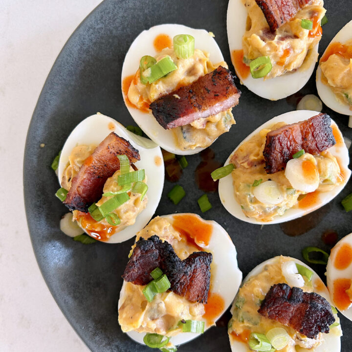 hard boiled eggs with bacon and green onion on a black plate