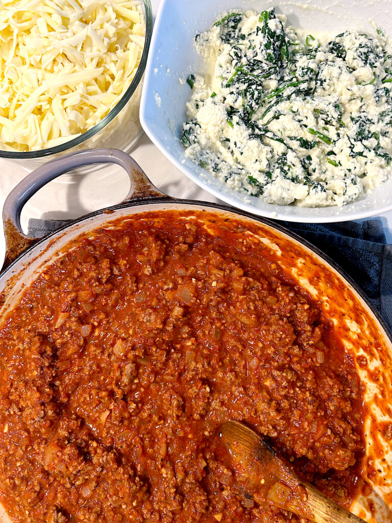 a pan with tomato meat sauce, and a bowl of ricotta cheese and spinach on the side
