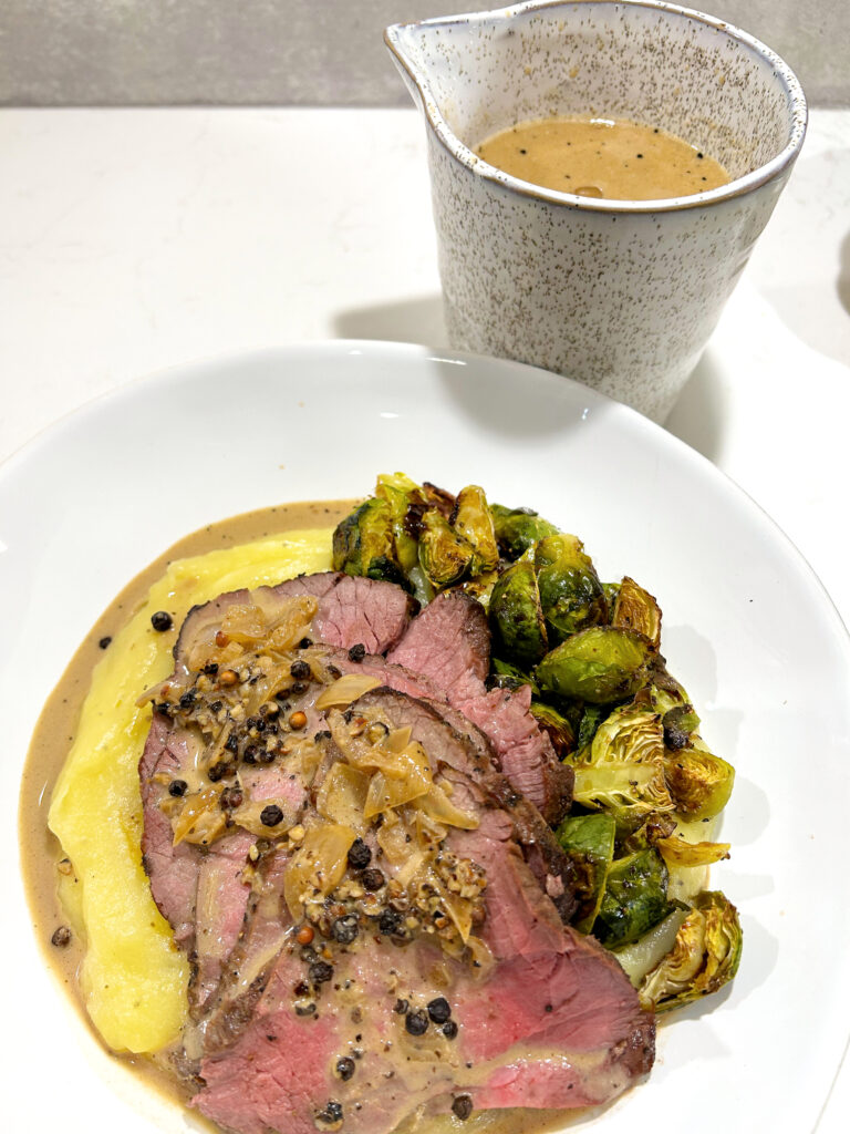 meat and mashed potatoes on a white plate with a cup of sauce.