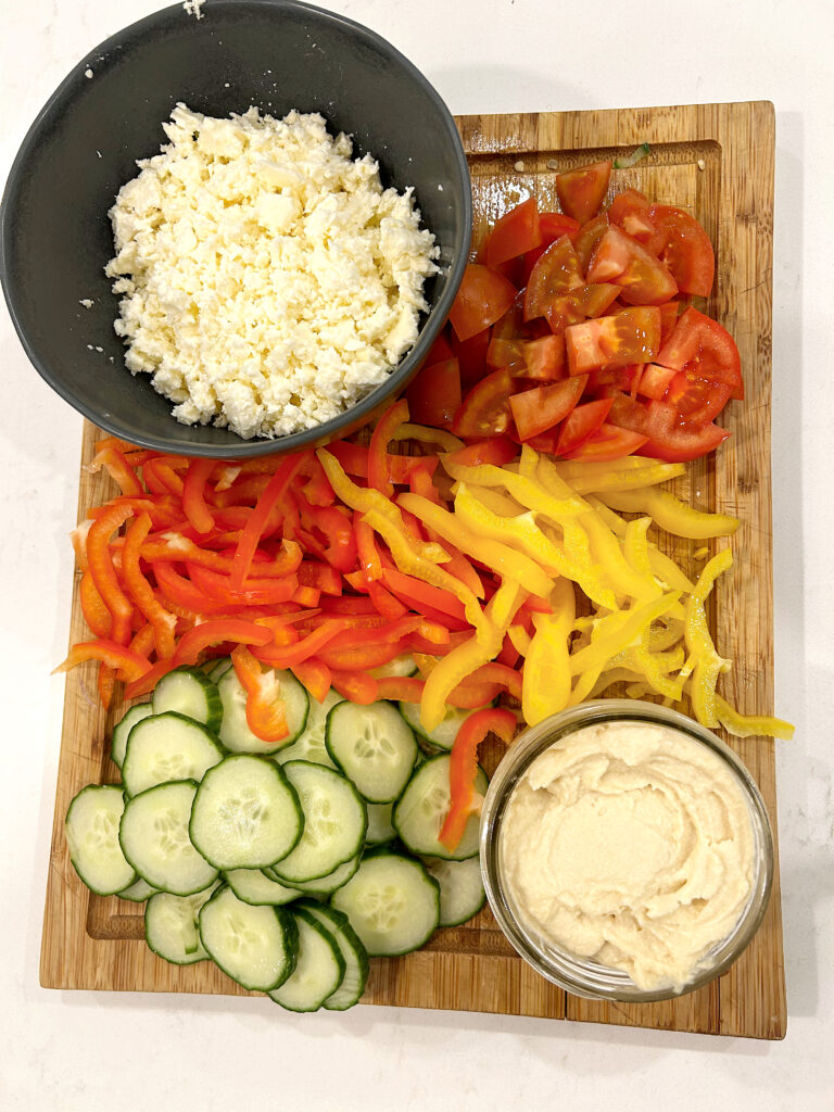 chopped vegetables, feta and hummus on a wood board