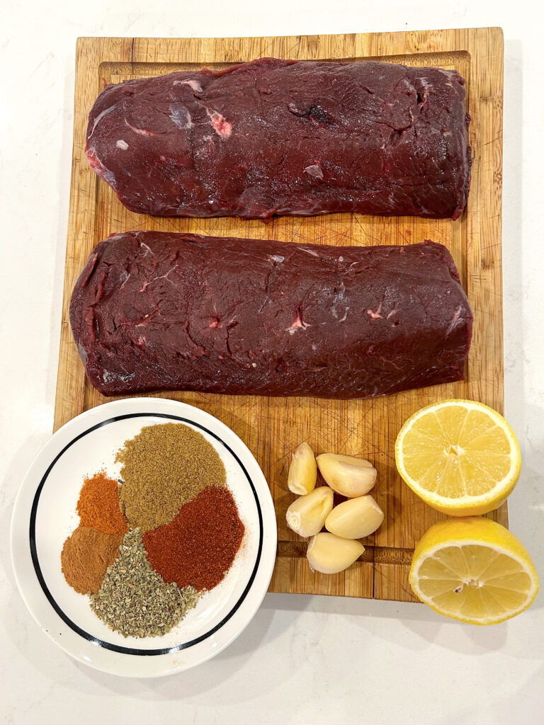 raw venison meat on a cutting board with lemon and spices