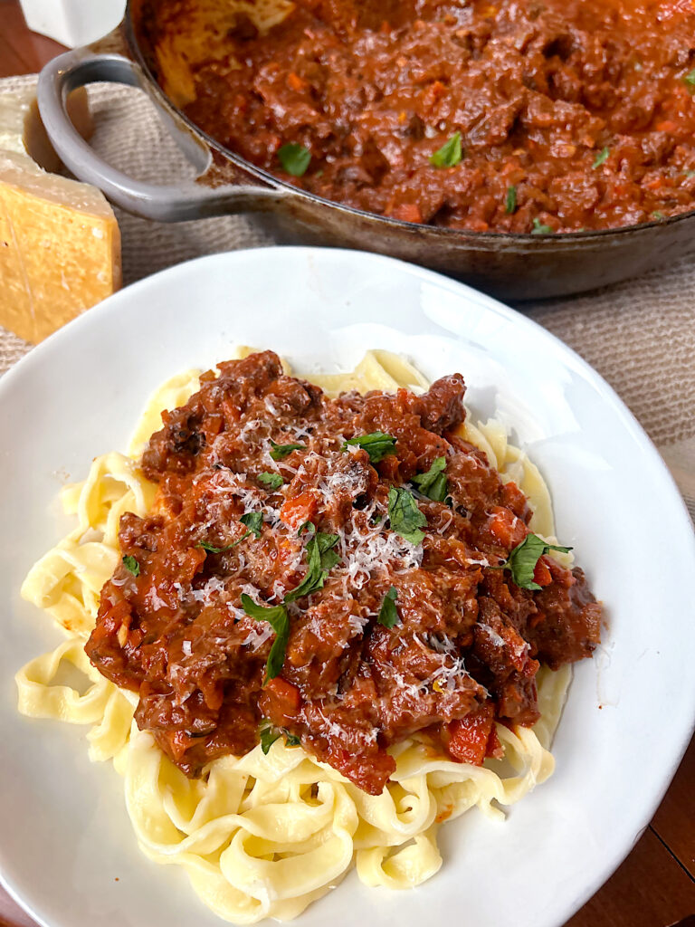 a white bowl with linguini pasta and a tomato bolognese sauce