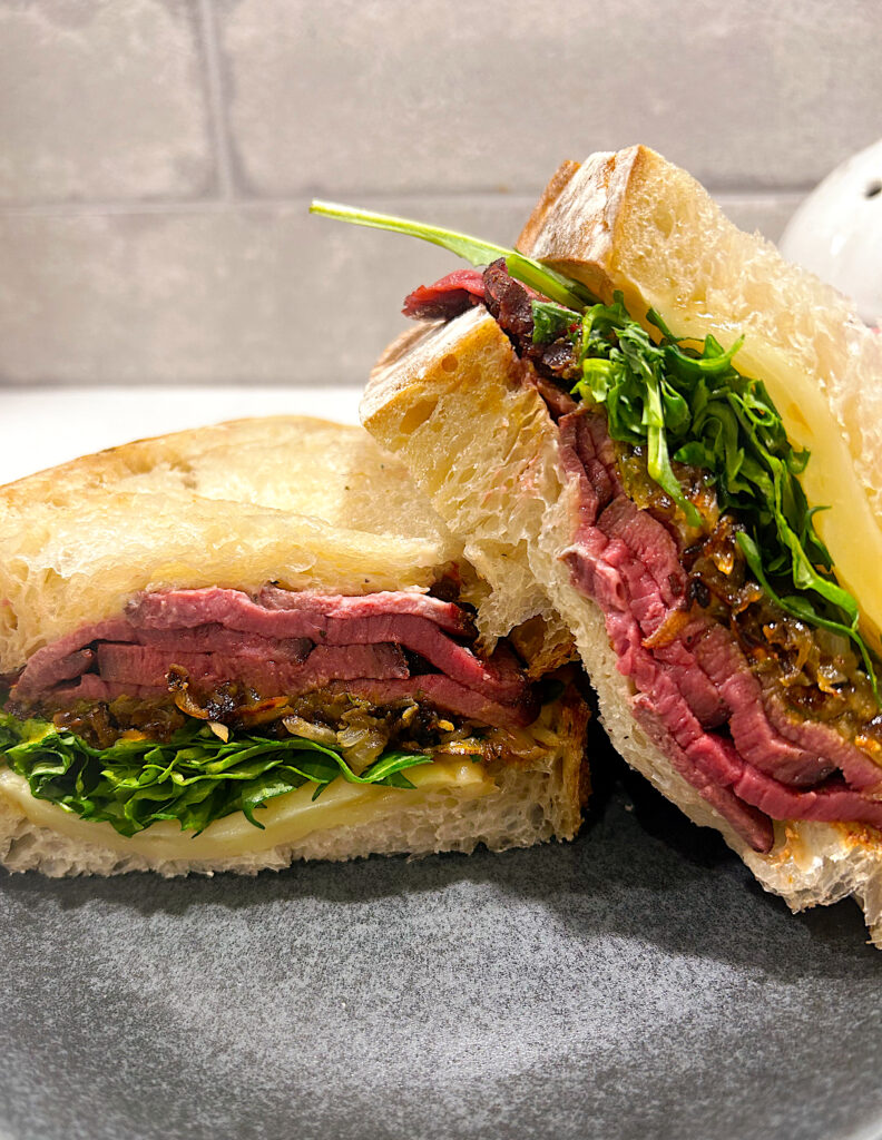 sandwich with steak, onions and arugula on a grey plate