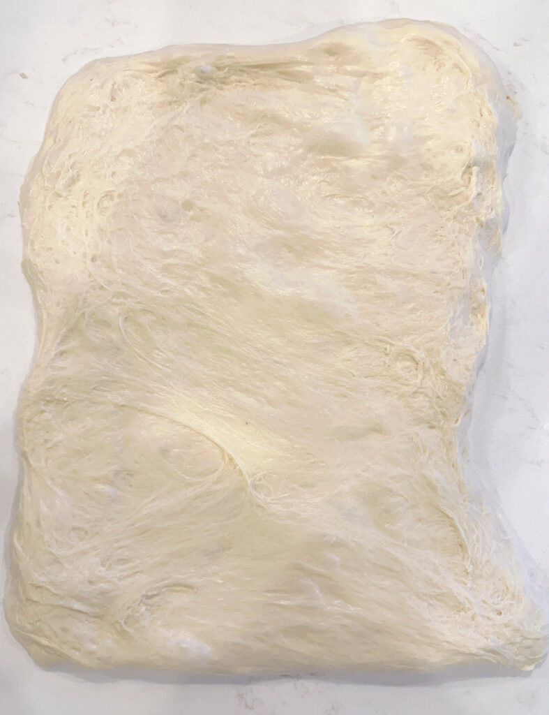  dough stretch into a rectangle on a white counter