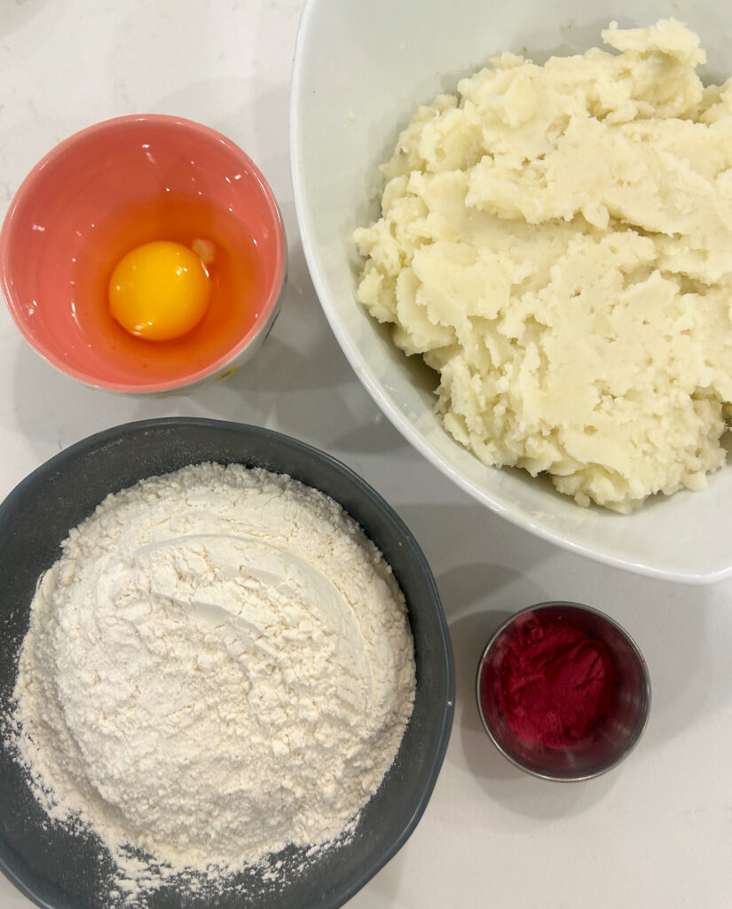 potatoes, flour and an egg in bowls on a white counter