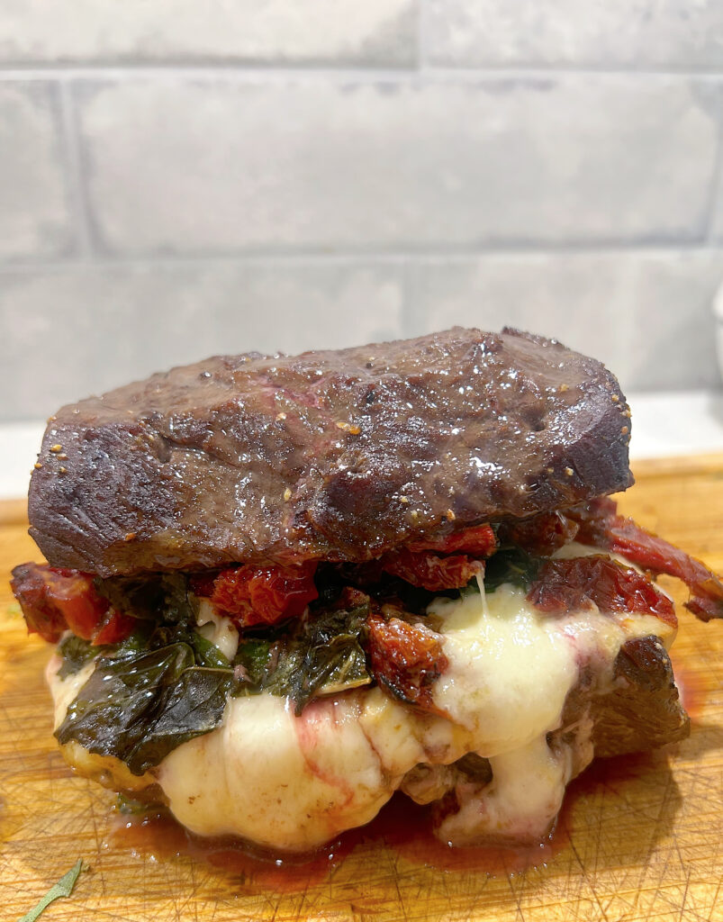 venison roast with tomato basil and cheese on a wood board