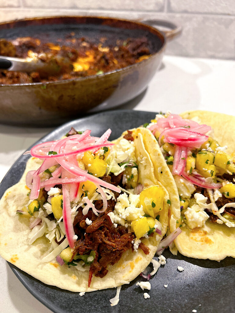tacos with shredded venison, pineapple and pickled onions on a black plate