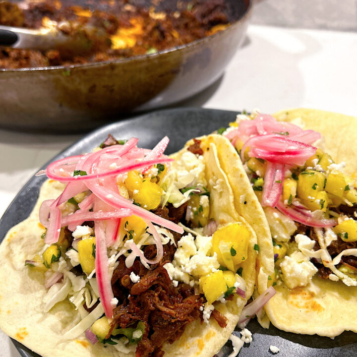 tacos with shredded venison, pineapple and pickled onions on a black plate