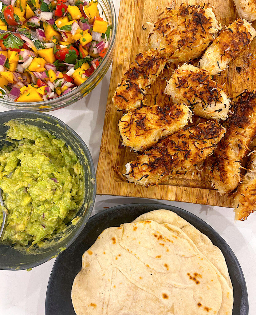fish. tortillas, guacamole and salsa on a white counter