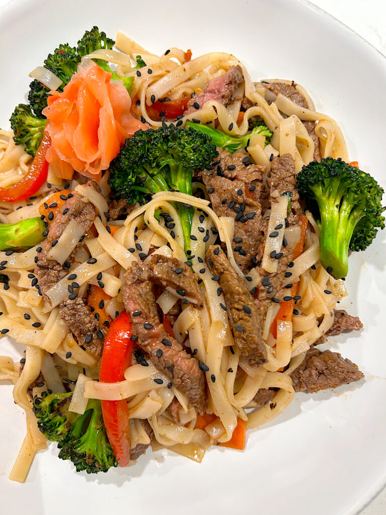 rice noodles with vegetables and beef in a white bowl