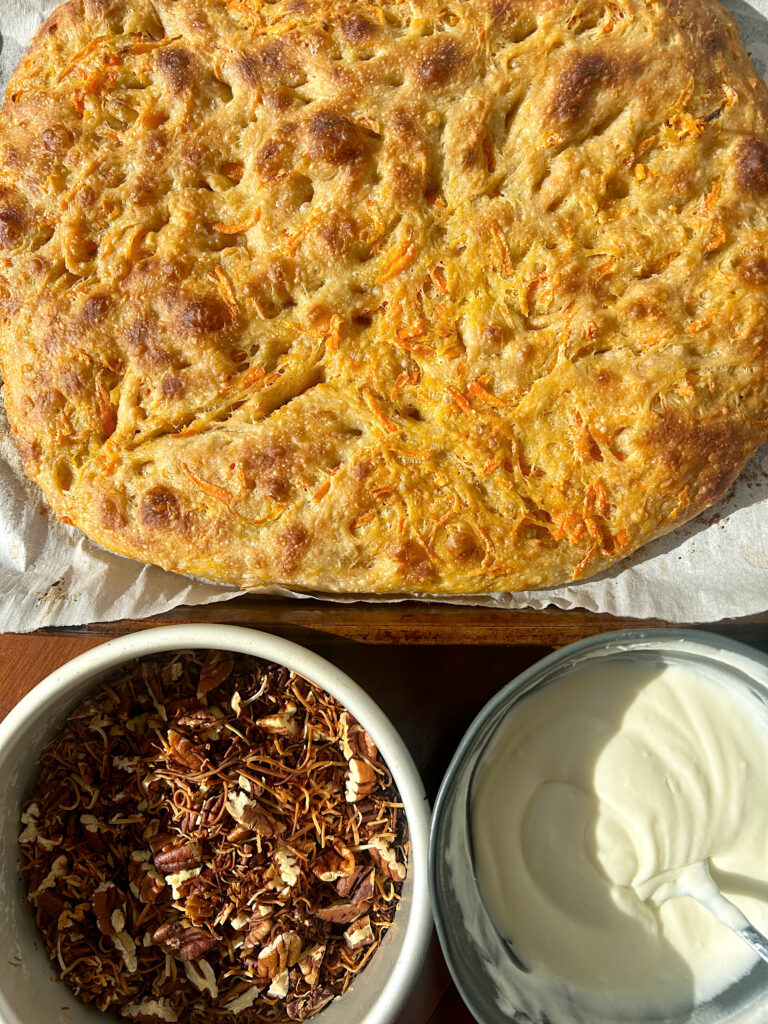 a loaf of focaccia bread with a bowl of cream cheese icing and toasted nuts on the side
