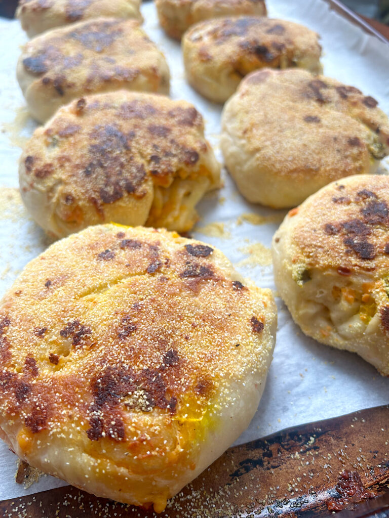 fresh baked english muffins with cheese and jalepenos on a baking sheet