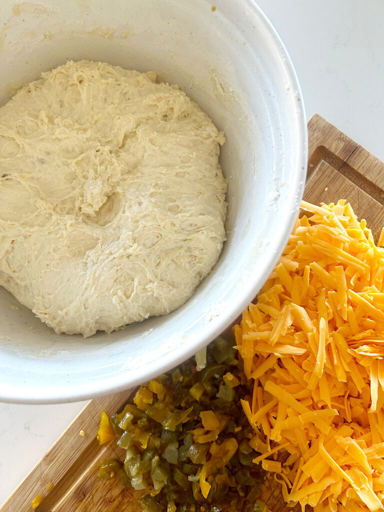 bread dough in a bowl with grated cheese and jaepenos on the side