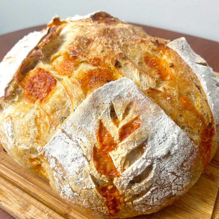 loaf of fresh cheesy sourdough bread on a wood board