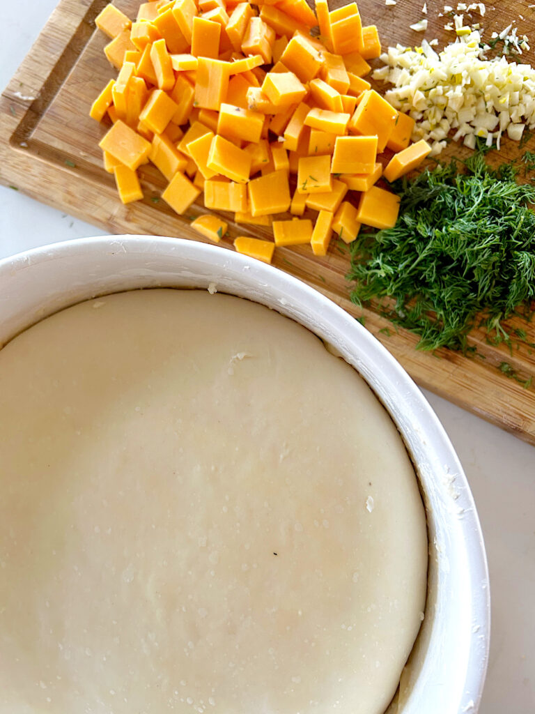 bowl of proofing dough and cheese and dill on a wood board