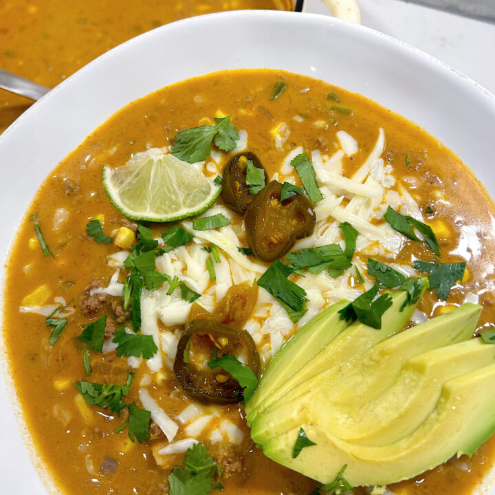white chili with avocado and cheese on top in a white bowl