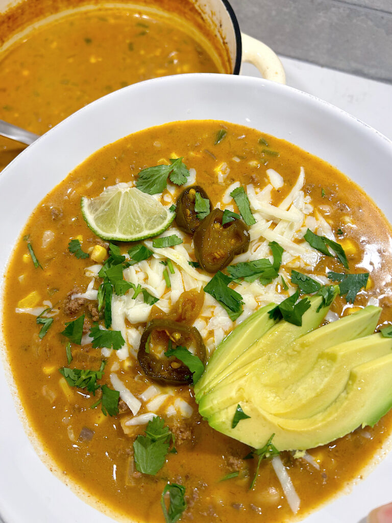 venison chili in a white bowl with avocado and cheese on top