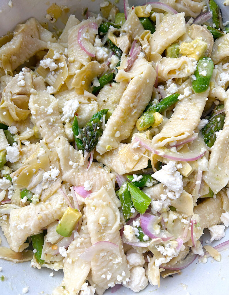 pasta in a bowl with asparagus, avocado, red onion and feta cheese