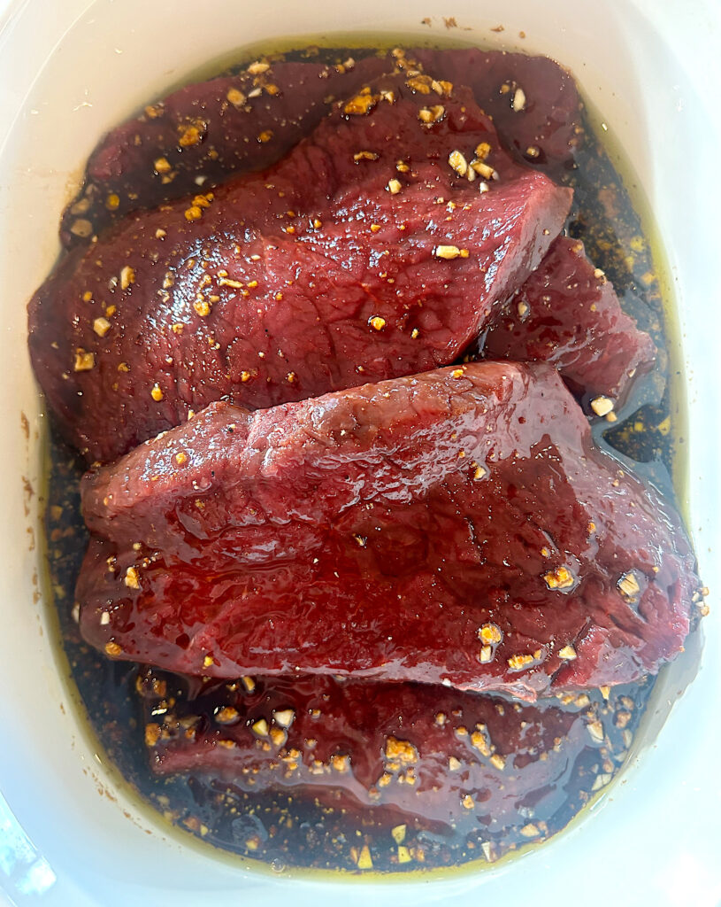 raw steaks in a balsamic marinade in a white casserole dish