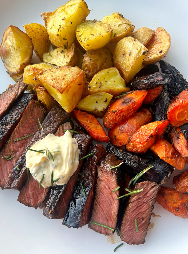 sliced steak, potatoes and carrots on a white plate with rosemary butter