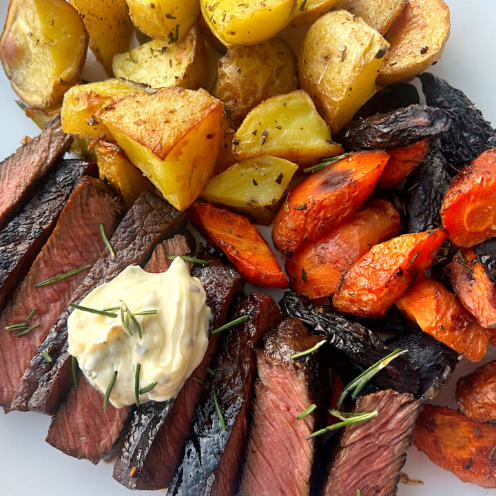 sliced steak, potatoes and carrots on a white plate with rosemary butter