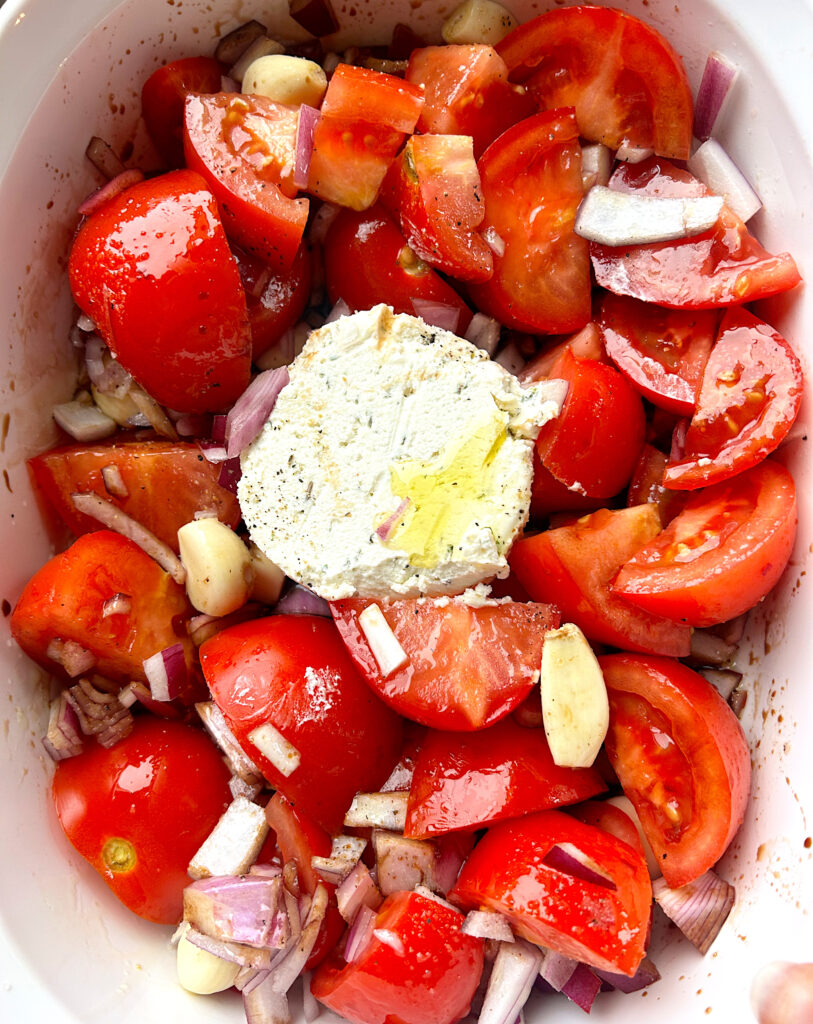 tomatos, garlic and a wheel of cheese in a baking dish