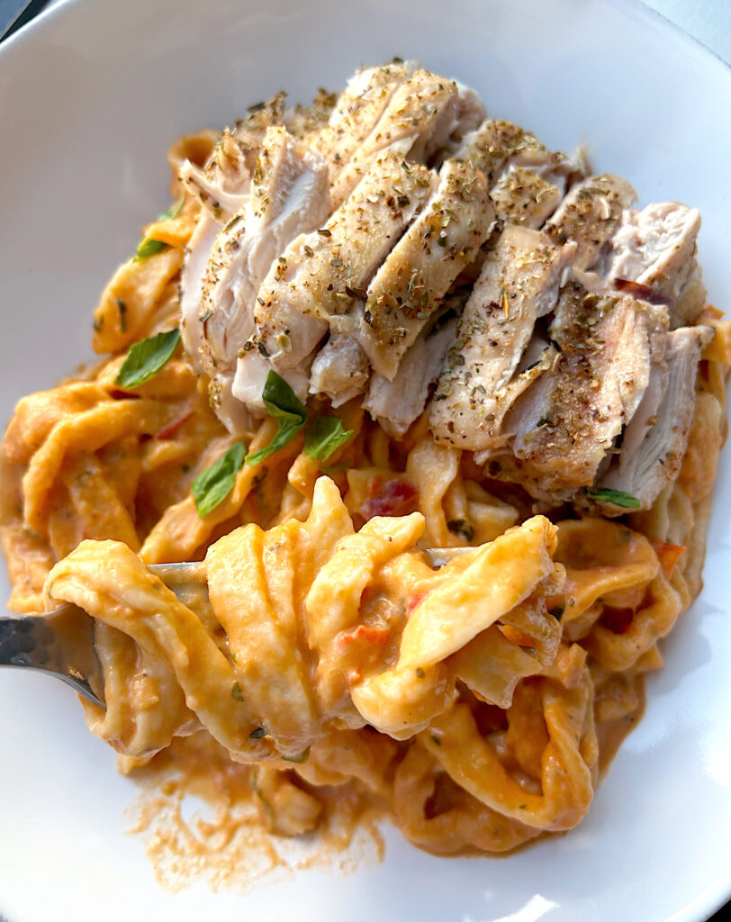 pasta with romato sauce and chicken thighs on top in a white bowl