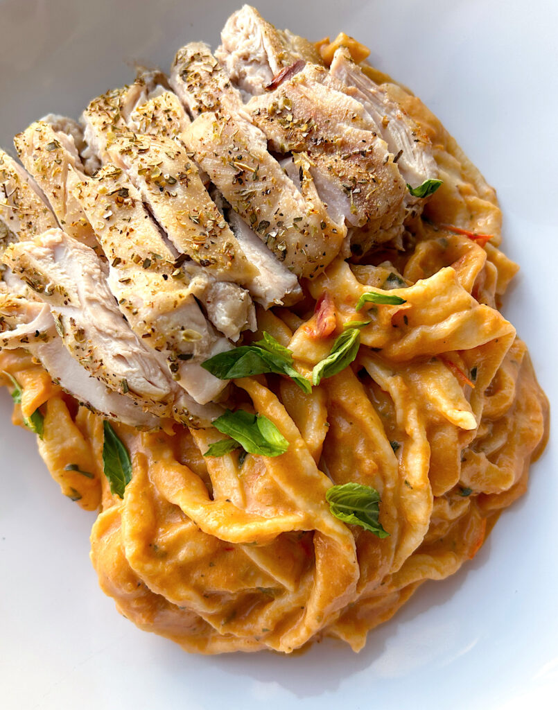 fresh bowl of pasta with red suace and chicken thighs on top