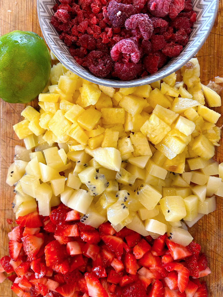 chopped strawberries, pineapple, kiwi and raspberries on a wood cutting board