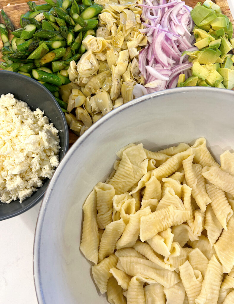 bowl of pasta with chopped vegetables on a wood board beside