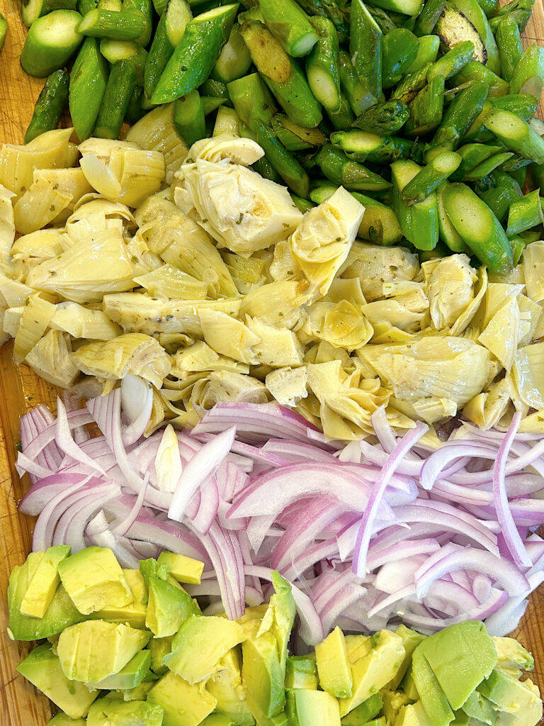 aspargus, artichokes, avocado and red onion on a wood board