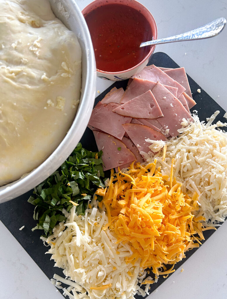 bread dough in a bowl with ham, cheese and basil on the side
