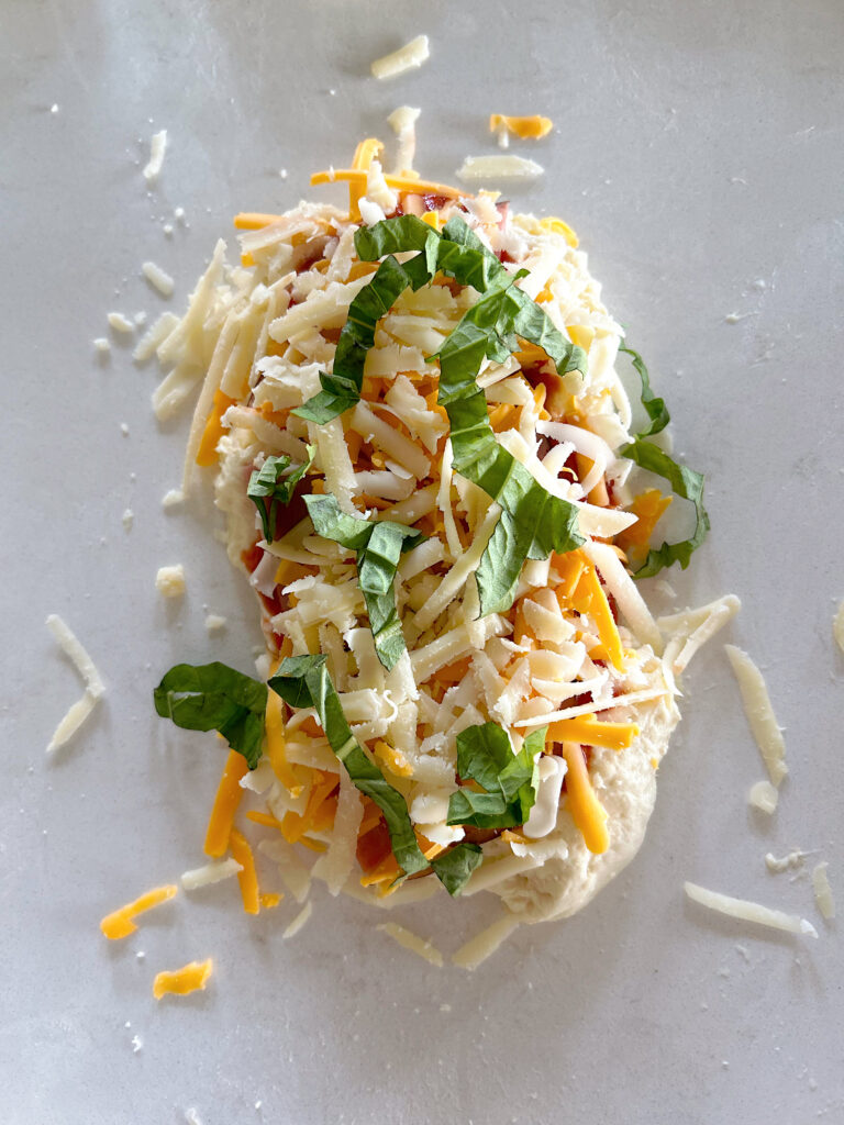 bread dough, topped with pizza sauce,, cheese and basil on a white counter