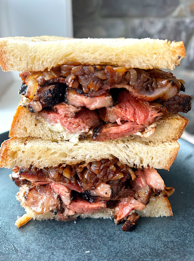 sandwich cut in half with steak and caramelized onions on a blue plate