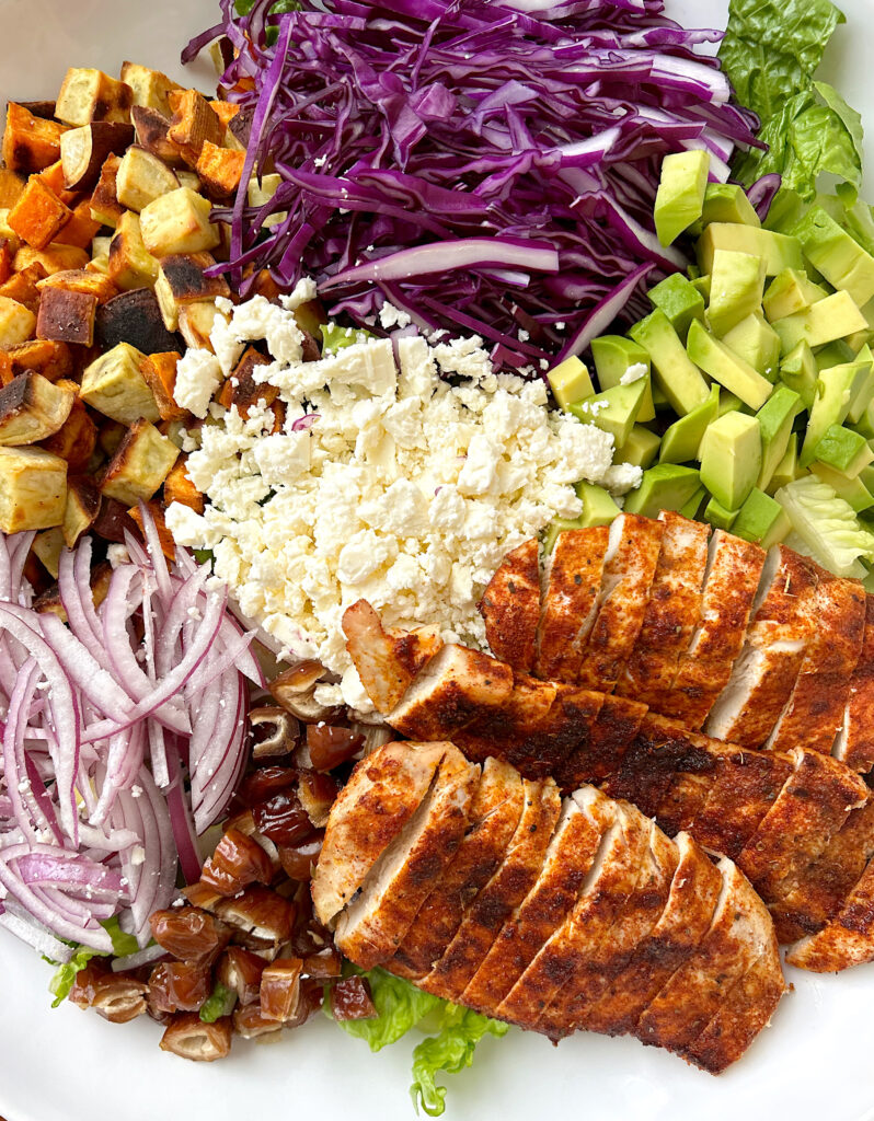 white bowl with lettuce, sweet potatoes, feta cheese, avocado and blackened chicken