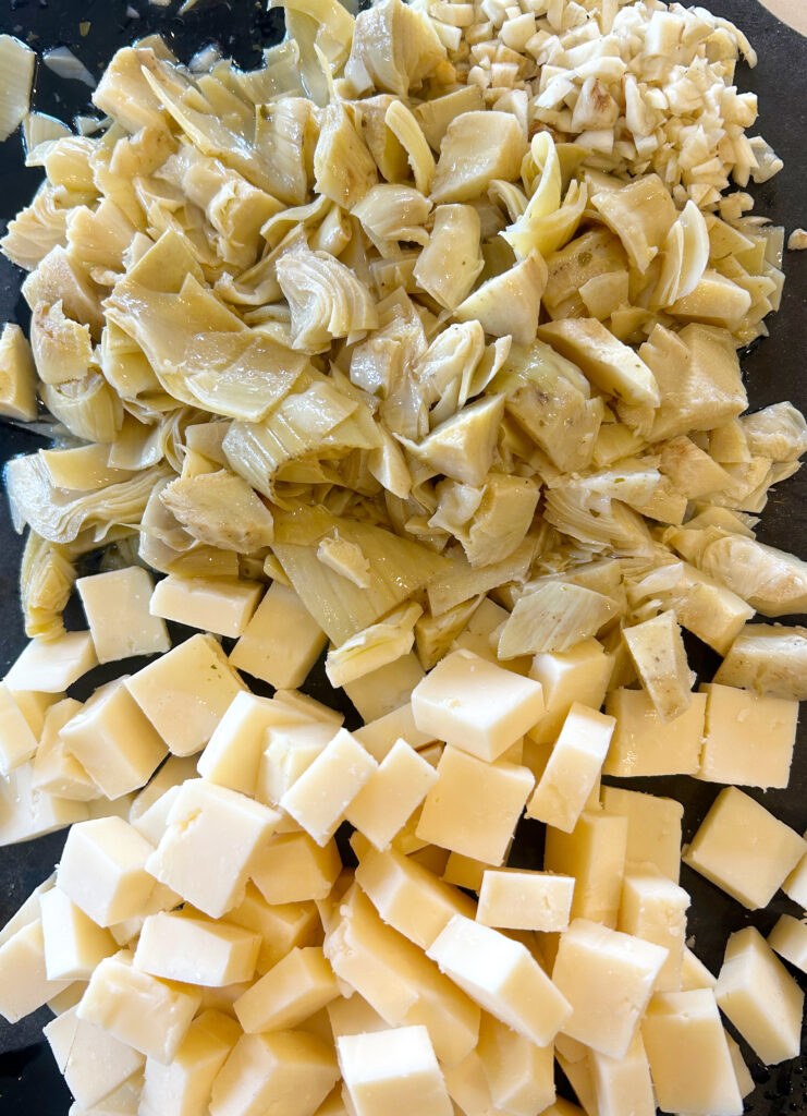 cubed cheese and chopped artichokes on a black cutting board