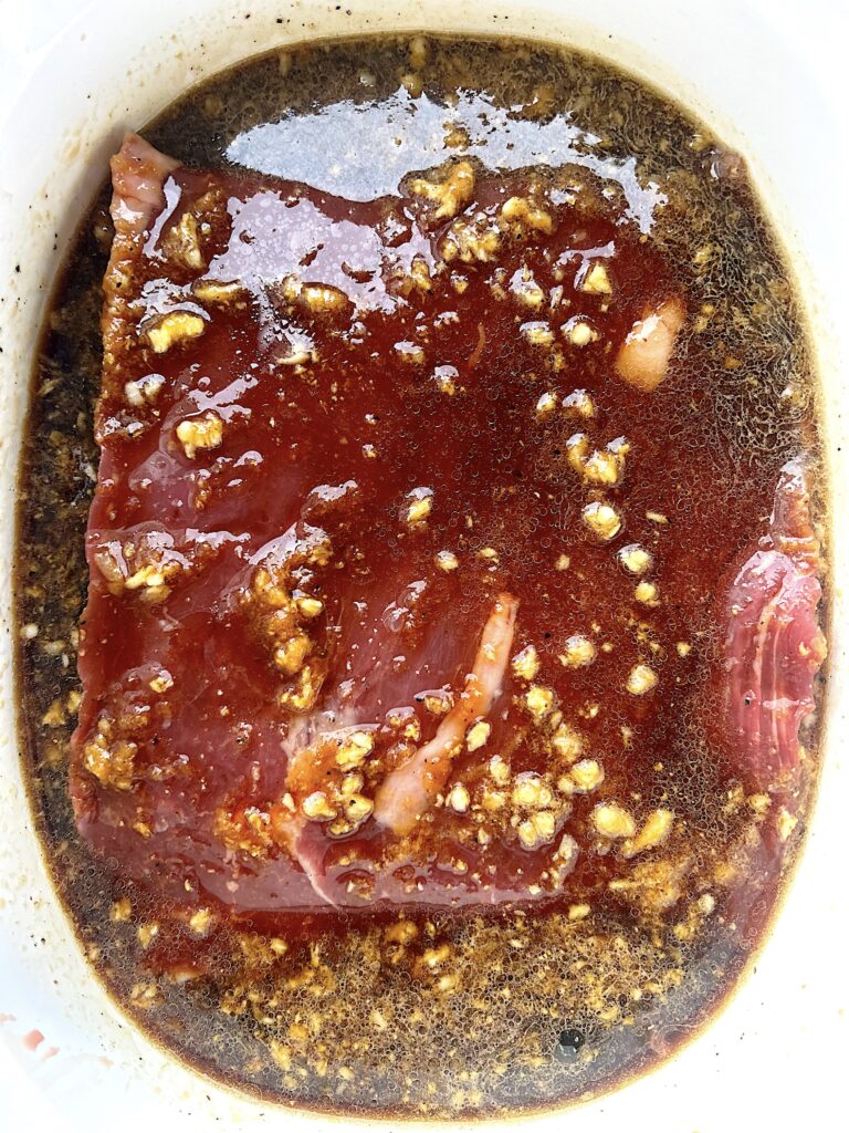 piece of raw flank steak sitting in a soy marinade