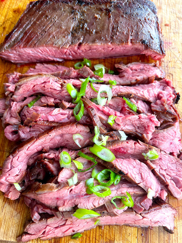 thinly sliced flank steak on a wood board