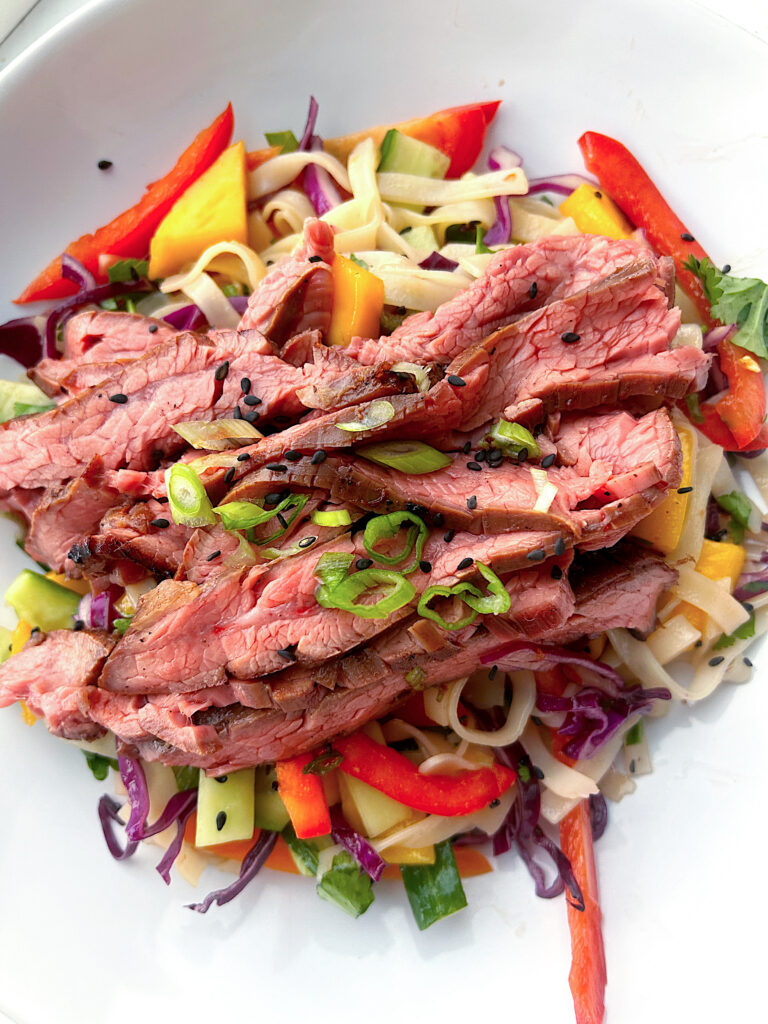 stiny sliced flank steak served over a rice noodle salad