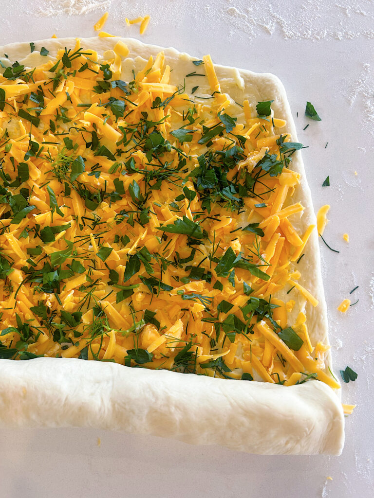 bread dough rolled out with cheese and fresh hearbs on top