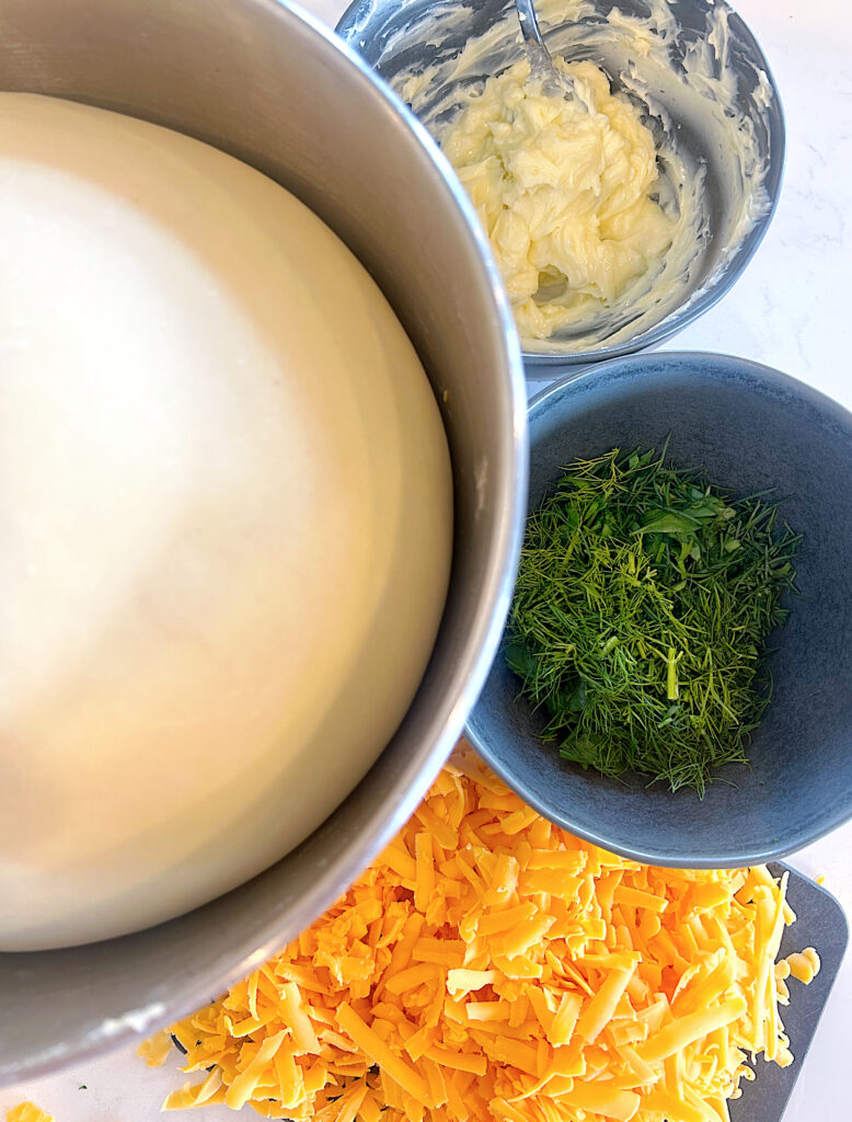 ball of dough with bowls of fresh herbs, butter and cheese beside