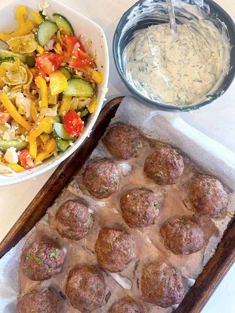 meatballs on a baking sheet with a bowl of greek salad 