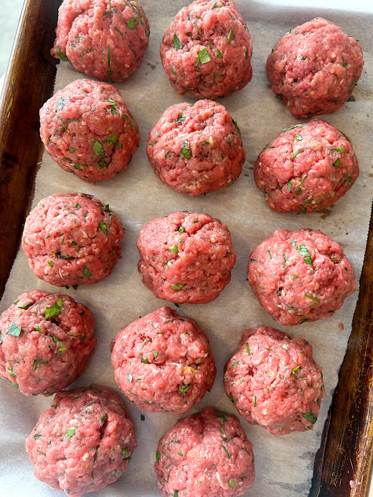 uncooked greek meatballs on a baking sheet 
