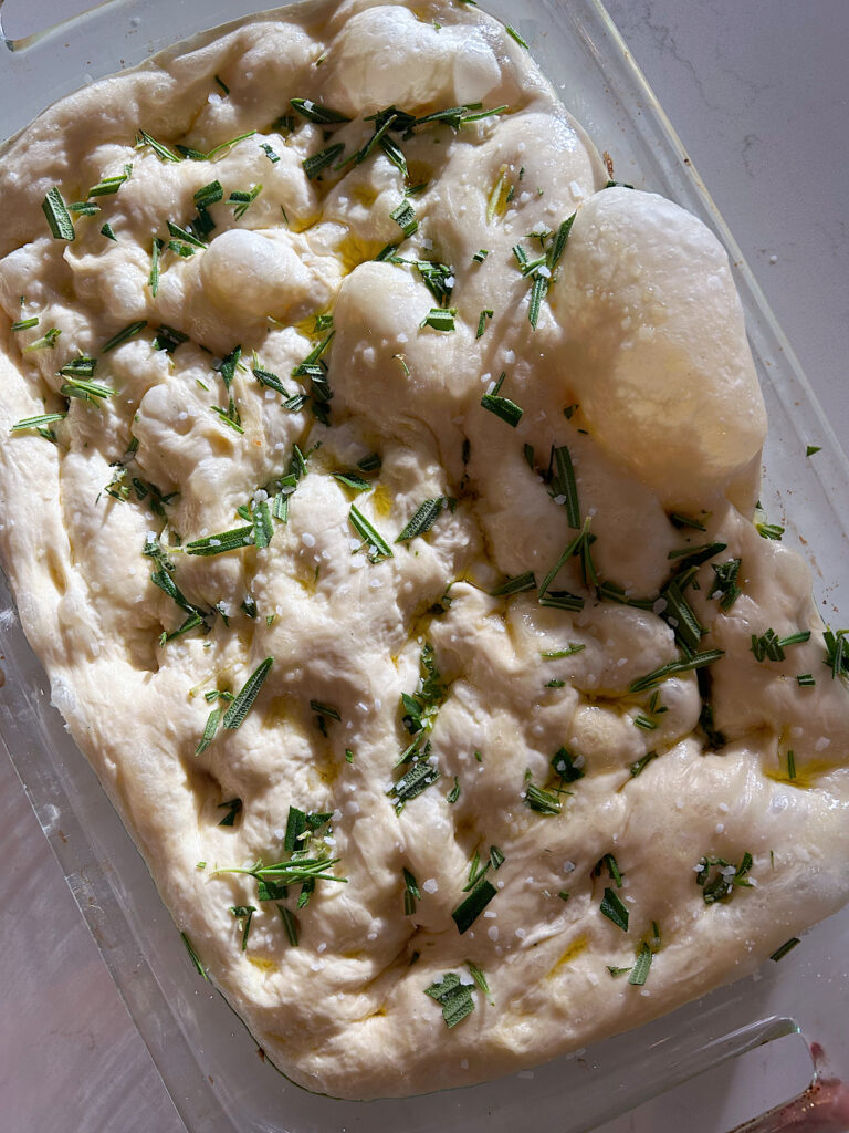unbaked focaccia bread with rosemary in a glass baking dish