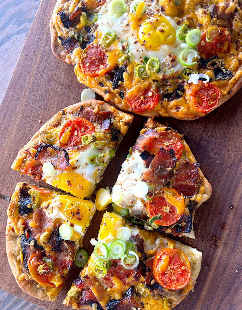 breakfast pizzas on a wood board with eggs, bacon and cheese