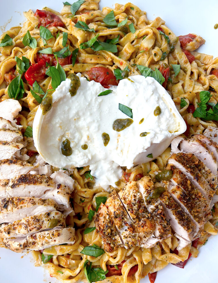 tomato and pesto pasta with burrata cheese and chicken breast on top