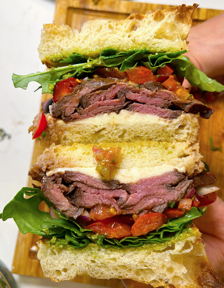 steak sandwich cut in half with mozarella, tomato and arugula