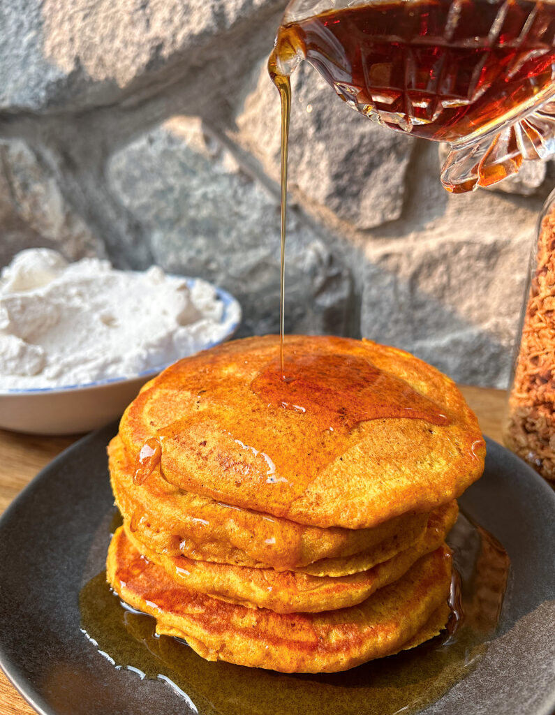 stack of pumpkin pancakes with maple syrup being poured on top